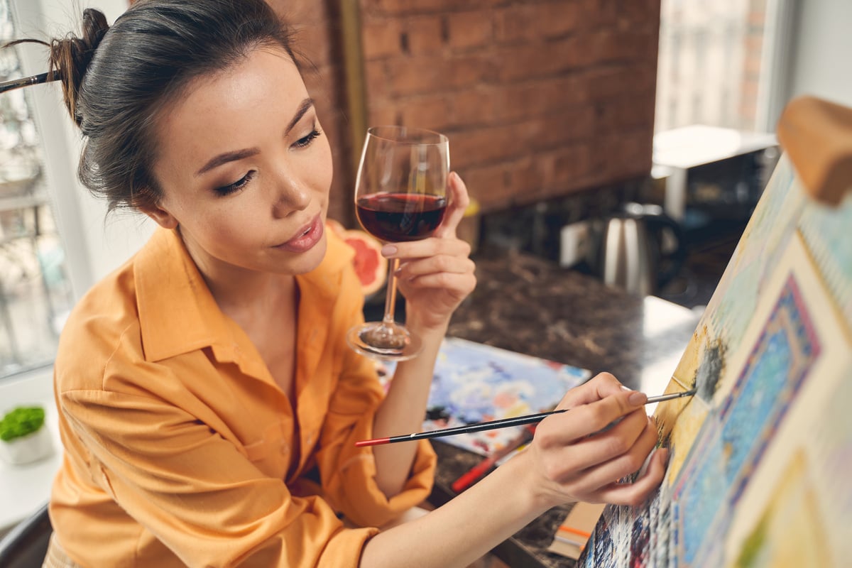 Beautiful lady drinking wine and painting on canvas